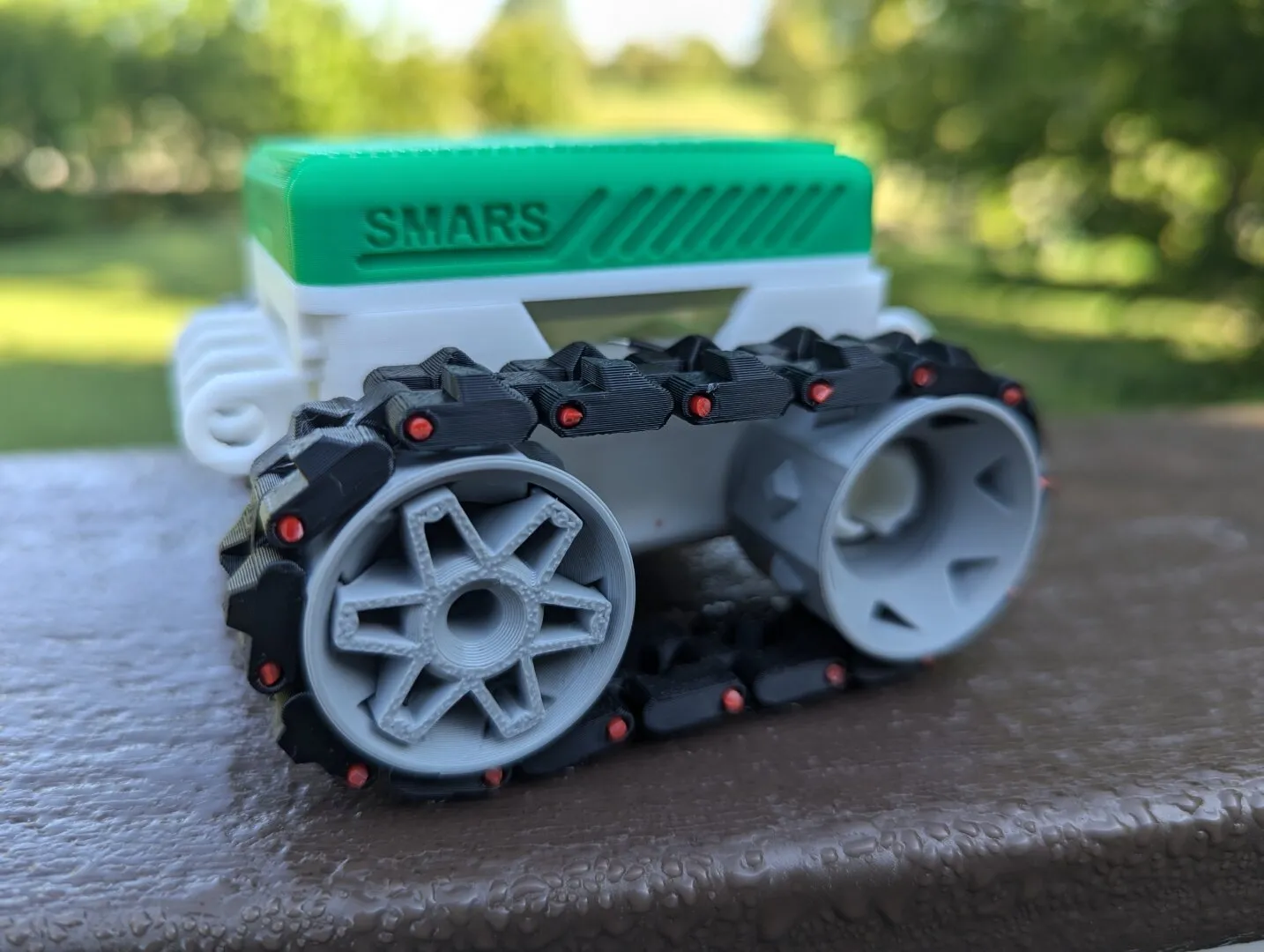 A small 3D printed rover style robot. It is white with a green top and black tank treds.